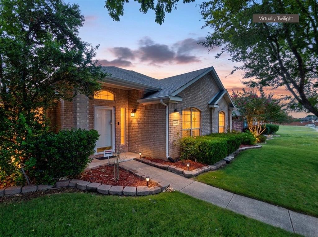 Brick exterior with a gabled roofline, arched windows, manicured landscaping, concrete walkway, and integrated exterior lighting