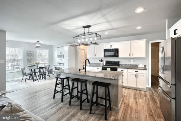 a kitchen with stainless steel appliances granite countertop a stove top oven a refrigerator a dining table and chairs with wooden floor