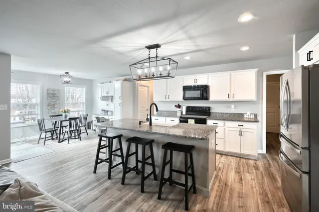 a kitchen with stainless steel appliances granite countertop a stove top oven a refrigerator a dining table and chairs with wooden floor