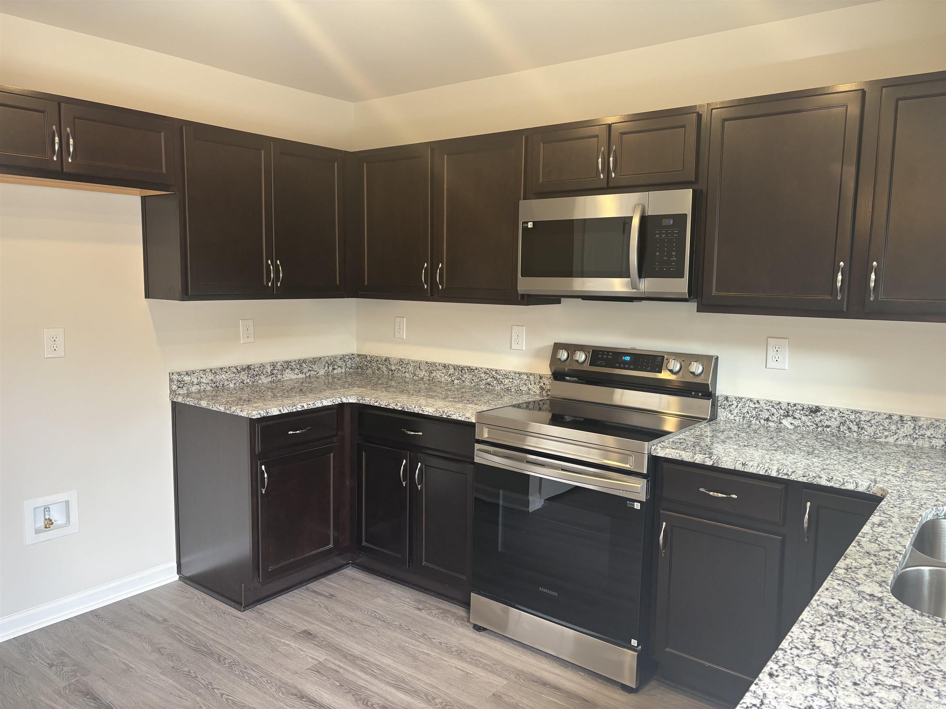 201 Kc Lane Aynor, SC 29511 - Photo 3 of 8 Kitchen with appliances with stainless steel finishes, light stone countertops, dark brown cabinets, and light wood-type flooring