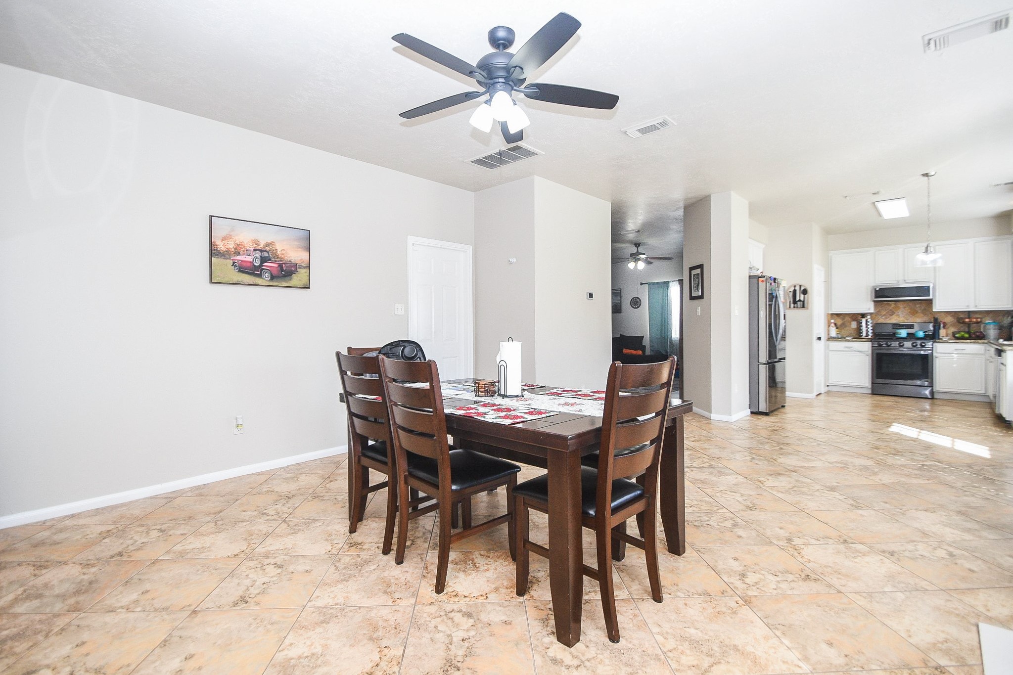 14407 Andrea Way Lane Houston, TX 77083 - Photo 13 of 29 This photo showcases a spacious dining area with tile flooring, modern ceiling fan. The open layout leads to a bright kitchen featuring stainless steel appliances and white cabinetry, creating an inviting space for family gatherings.