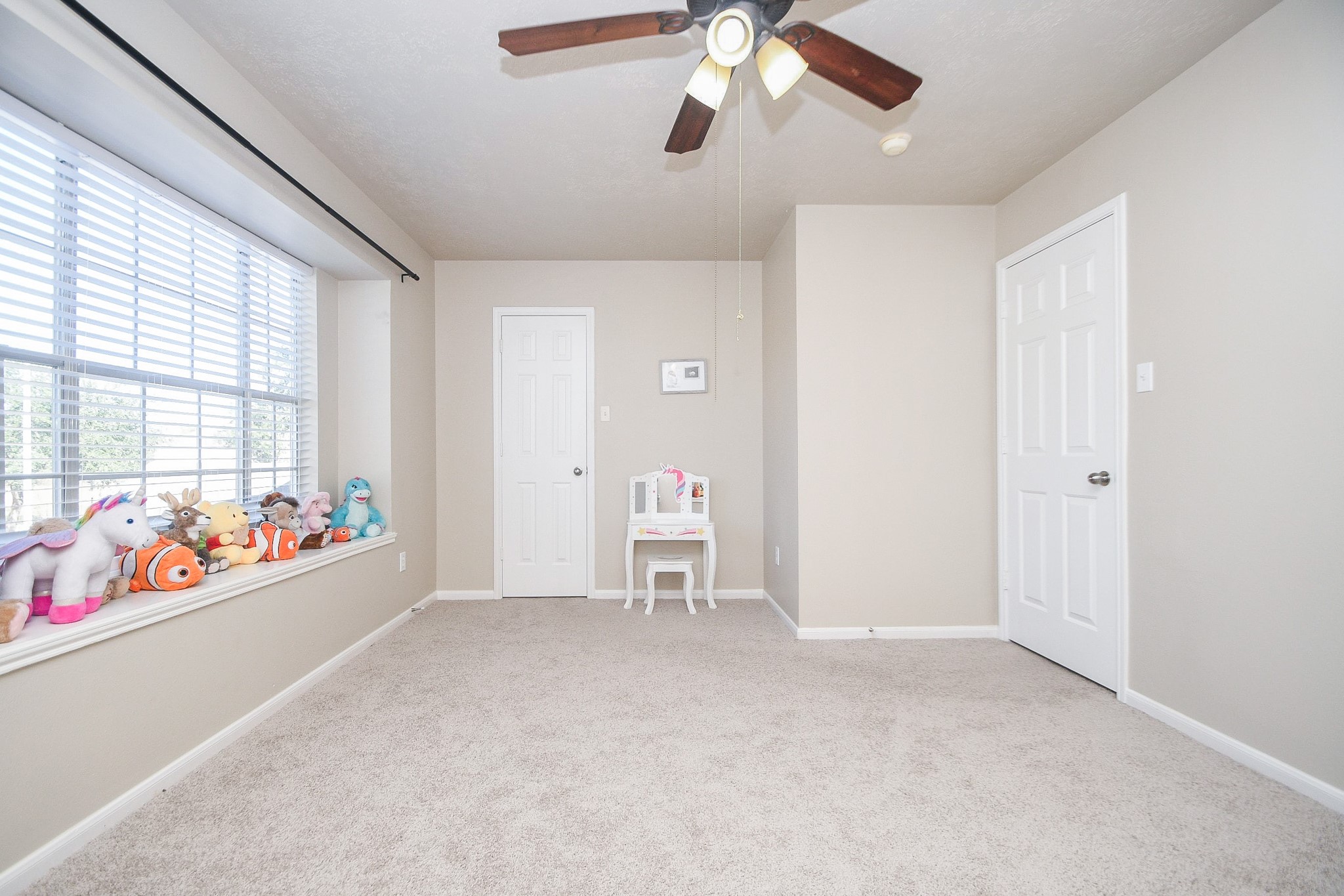 14407 Andrea Way Lane Houston, TX 77083 - Photo 15 of 29 Bright, neutral-toned room with plush carpet and a large window seat. Features a ceiling fan and two doors, ideal for a TV room or playroom.