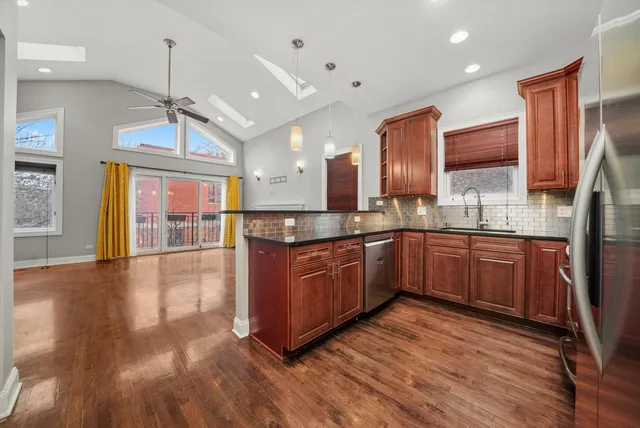 a kitchen with stainless steel appliances granite countertop wooden floors wooden cabinets a window and a sink