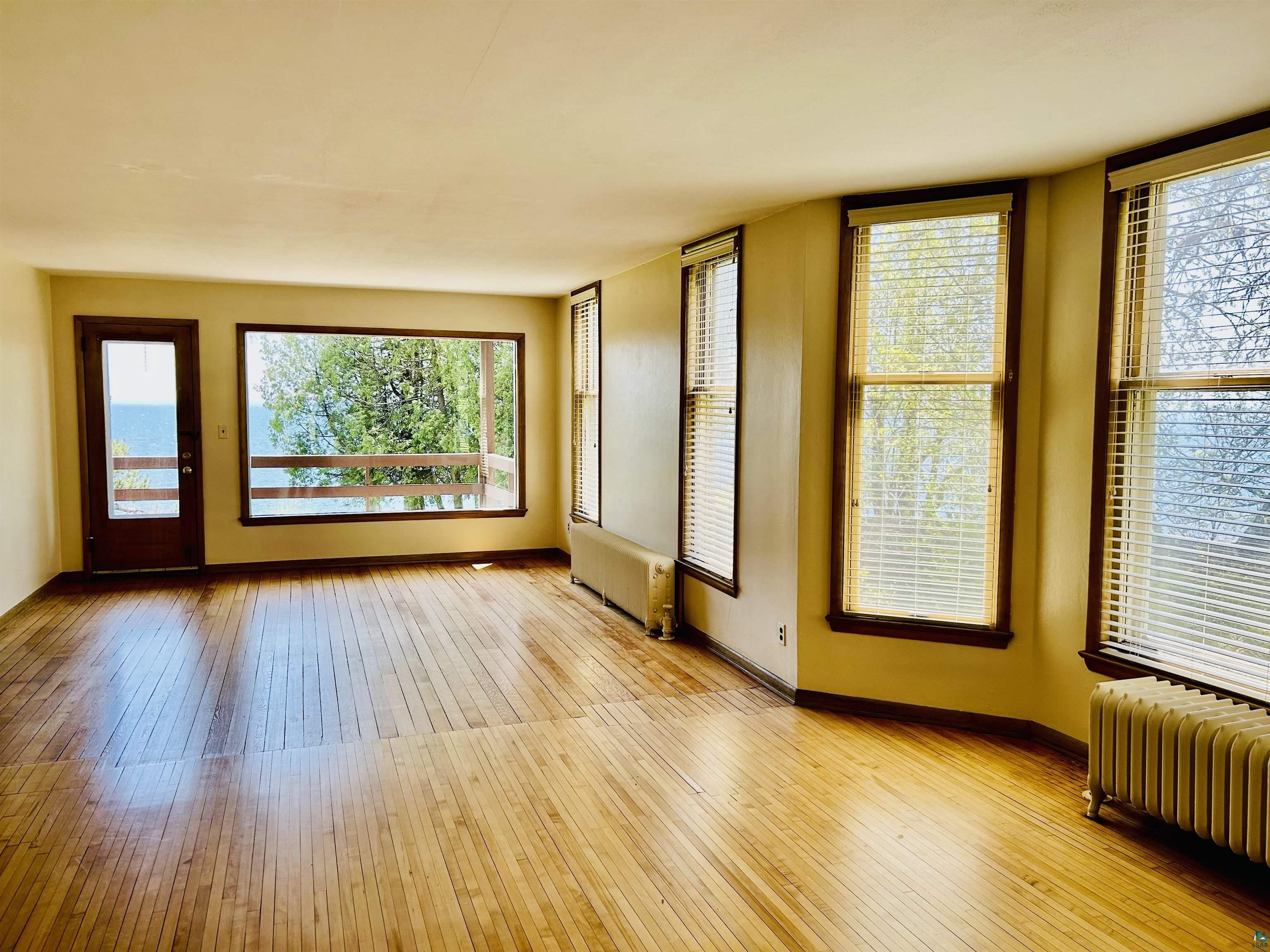 5090 London Road, Unit 1 Duluth, MN 55804 - Photo 17 of 54 Spacious interior featuring wood-finish flooring, multiple large windows with blinds, a glass-paneled exterior door, and a built-in radiator