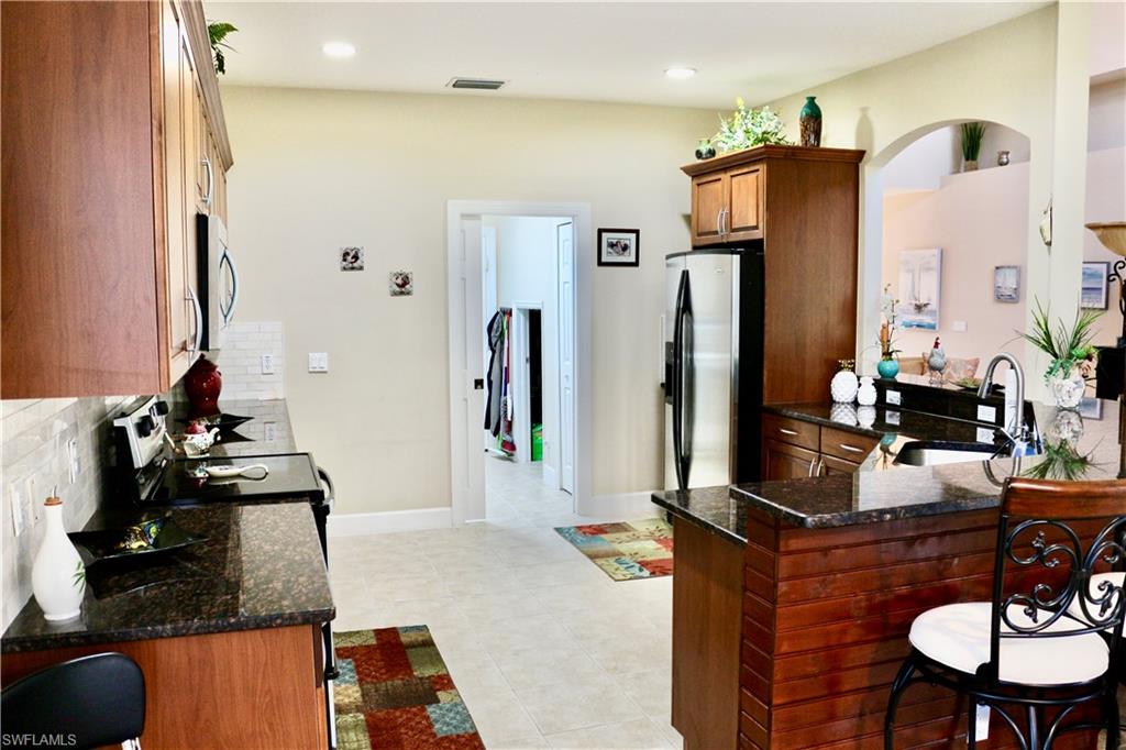 15474 Los Reyes Lane Naples, FL 34110 - Photo 9 of 36 a room with stainless steel appliances kitchen island granite countertop a refrigerator and a sink