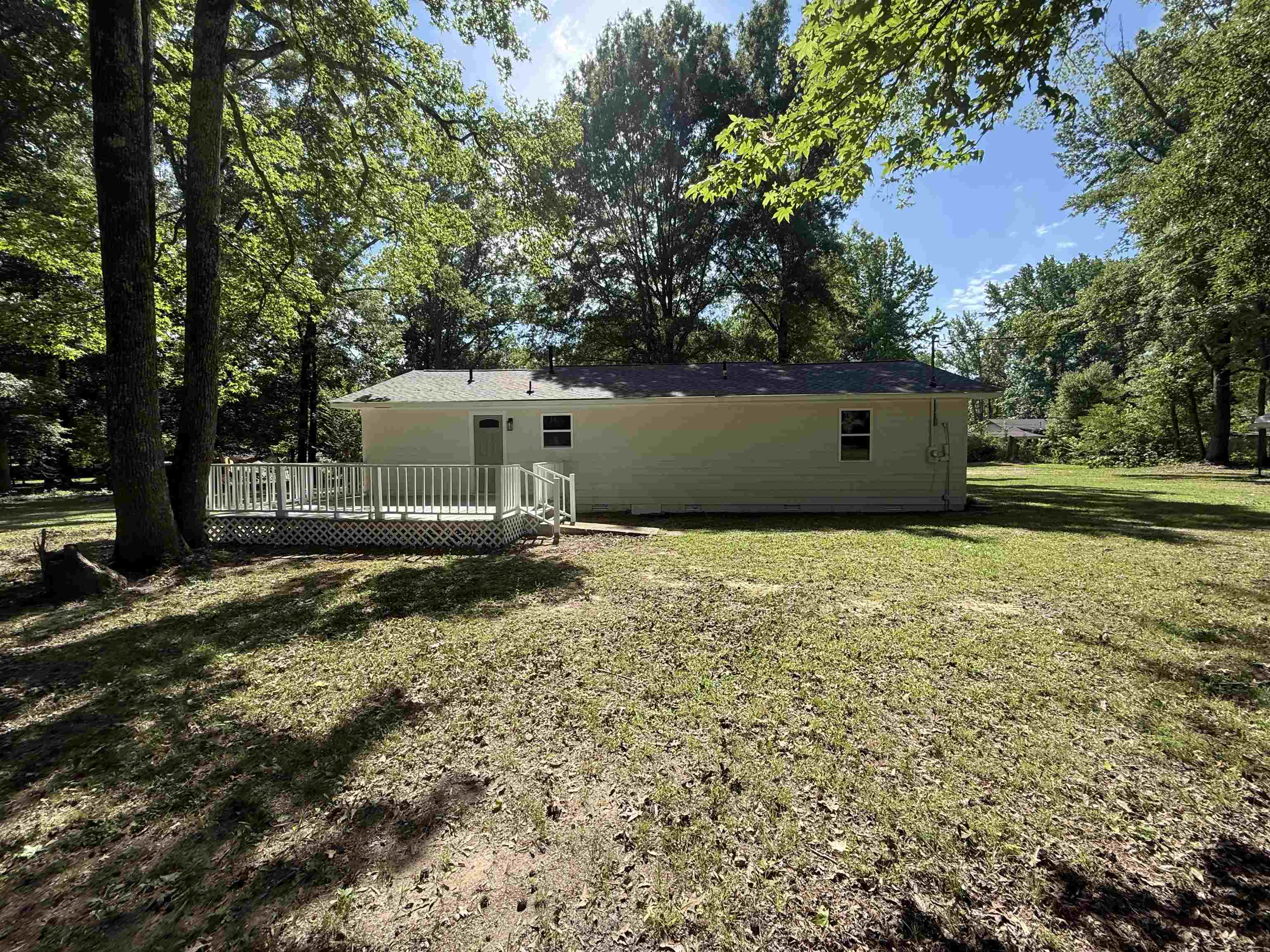 195 Poole Road Moscow, TN 38057 - Photo 20 of 21 Rear exterior featuring a white painted wood deck with lattice skirting and a privacy railing, set against a backdrop of mature trees