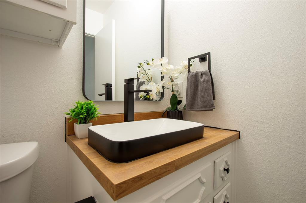 1205 Augusta Road Benbrook, TX 76126 - Photo 17 of 21 Powder room featuring a rectangular vessel sink with a matte black faucet, a wood-finish countertop, and a contemporary wall mirror