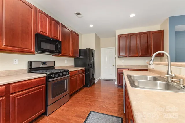 a kitchen with stainless steel appliances granite countertop a stove a sink dishwasher a refrigerator and a microwave oven with wooden floor