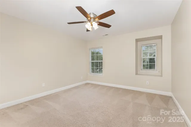 an empty room with ceiling fan and windows