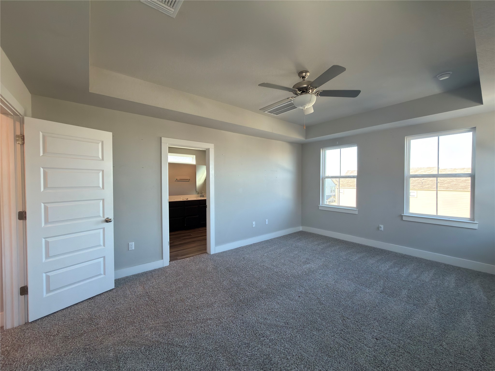7312 Acela Trail Austin, TX 78744 - Photo 11 of 26 Unfurnished bedroom featuring a raised ceiling, dark colored carpet, connected bathroom, and ceiling fan