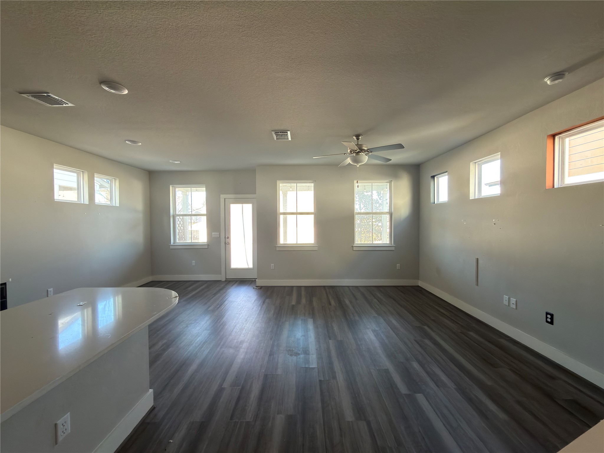 7312 Acela Trail Austin, TX 78744 - Photo 4 of 26 Unfurnished living room featuring a ceiling fan, dark wood-style flooring, healthy amount of natural light, and a textured ceiling