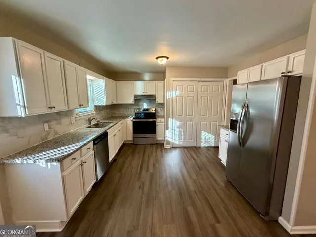 a kitchen with granite countertop a refrigerator a sink dishwasher a stove and white countertops with wooden floor