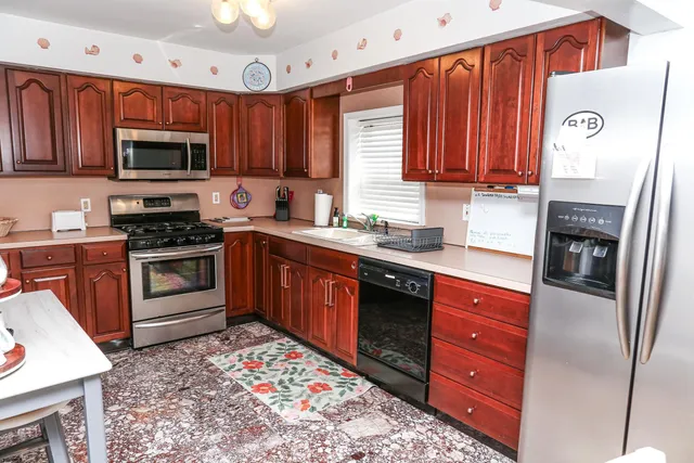 a kitchen with stainless steel appliances granite countertop a stove top oven a sink dishwasher and a refrigerator with wooden cabinets