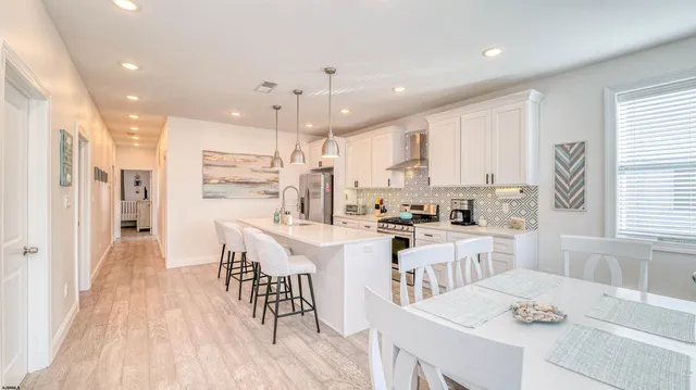 a kitchen with stainless steel appliances kitchen island granite countertop a refrigerator a stove a sink a dining table and chairs with wooden floor