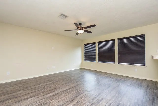 a view of an empty room with wooden floor and a ceiling fan