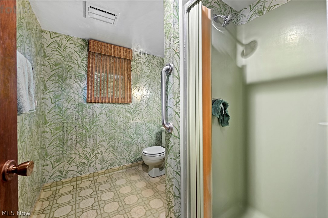 6451 Kungle Road Clinton, OH 44216 - Photo 22 of 34 Full bathroom featuring ceramic tile walls with botanical patterning, geometric tile flooring, toilet with chrome fixtures, pedestal sink area, and enclosed shower stall with sliding glass enclosure and chrome showerhead