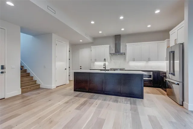 a kitchen with kitchen island granite countertop wooden floors stainless steel appliances a sink and a refrigerator