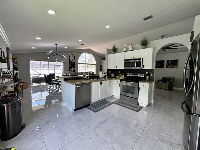 a kitchen with stainless steel appliances kitchen island granite countertop a refrigerator sink and white cabinets