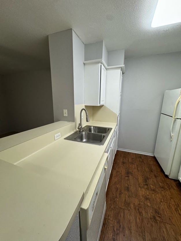 1305 West Villa Maria Road, Unit C107 Bryan, TX 77801 - Photo 8 of 19 Kitchen with light countertops, white cabinetry, a textured ceiling, dark wood finished floors, and freestanding refrigerator