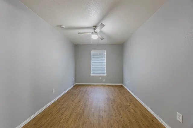 an empty room with wooden floor ceiling fan and windows