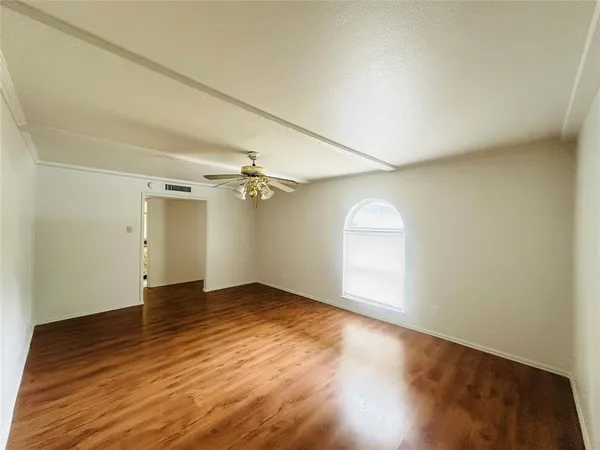 an empty room with wooden floor chandelier fan and windows