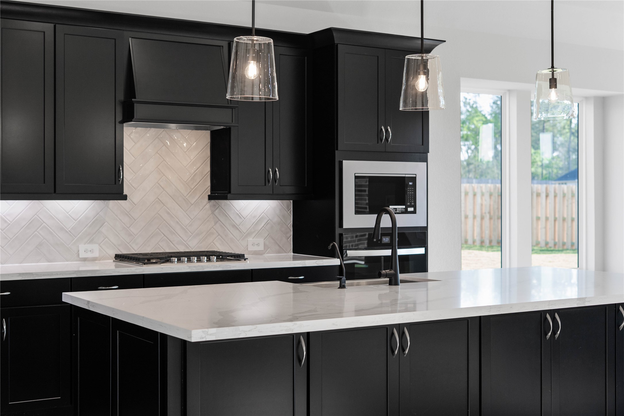2114 Rowl Street Montgomery, TX 77316 - Photo 24 of 50 This kitchen features dramatic midnight-black cabinetry (topped with elegant crown molding), pristine quartz countertops, and herringbone subway tile backsplash, creating a clean and contemporary aesthetic. Equipped with stainless steel appliances including a built-in oven, microwave, and modern range hood, this space offers both style and functionality.