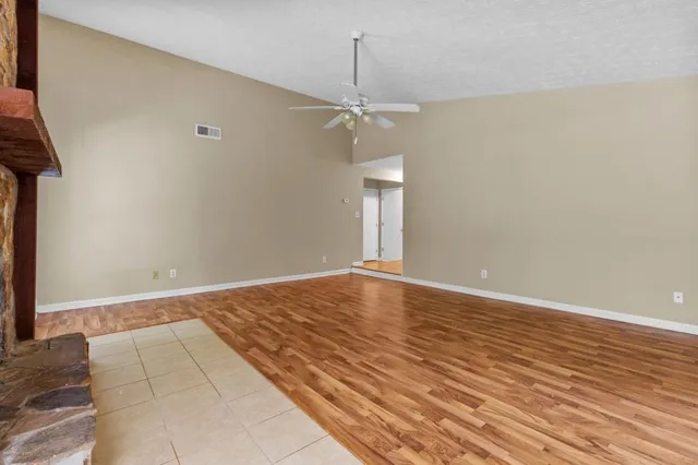 a view of an empty room with wooden floor and a ceiling fan
