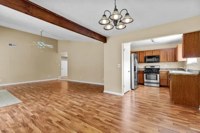 a view of an empty room and kitchen with wooden floor