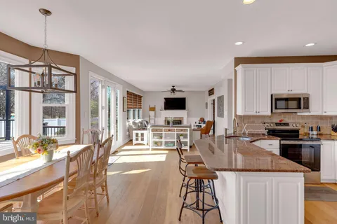 a kitchen with stainless steel appliances granite countertop a stove top oven a sink a dining table and chairs with wooden floor