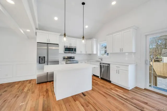 a kitchen with stainless steel appliances white cabinets a sink a stove a refrigerator and white cabinets with wooden floor