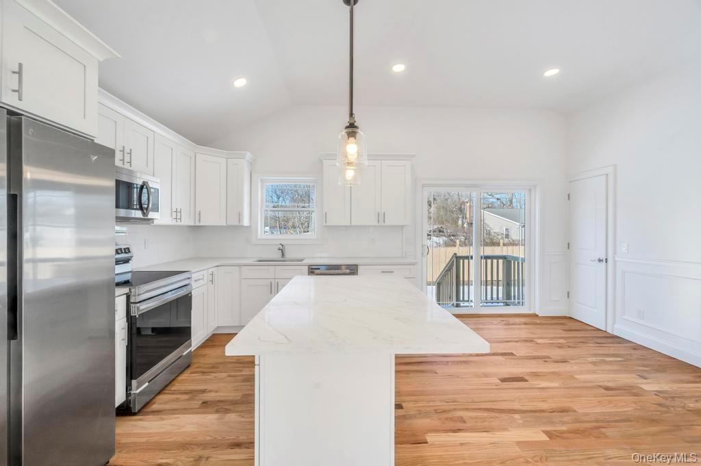 49 Barclay Road Mastic Beach, NY 11951 - Photo 18 of 33 a large kitchen with kitchen island a stove a sink a refrigerator white cabinets and wooden floor