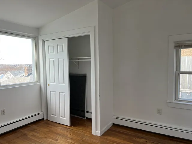 an empty room with wooden floor cabinet and windows