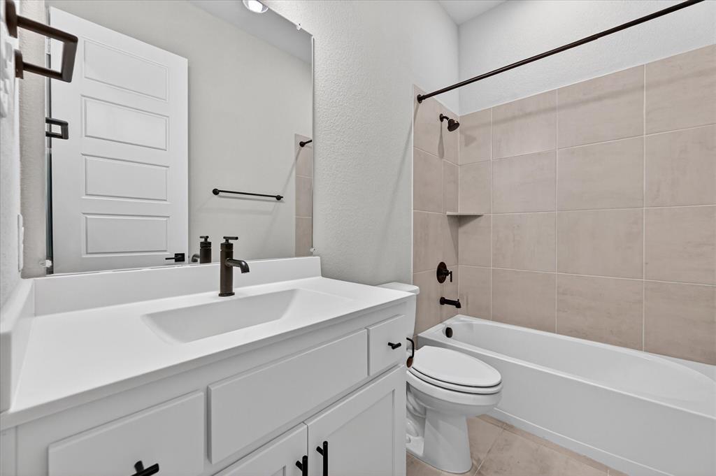 2237 Pika Road Northlake, TX 76247 - Photo 25 of 37 Bathroom featuring a white vanity with integrated sink, dark bronze fixtures, light-toned tile flooring, and a tiled shower-tub combination with a built-in niche