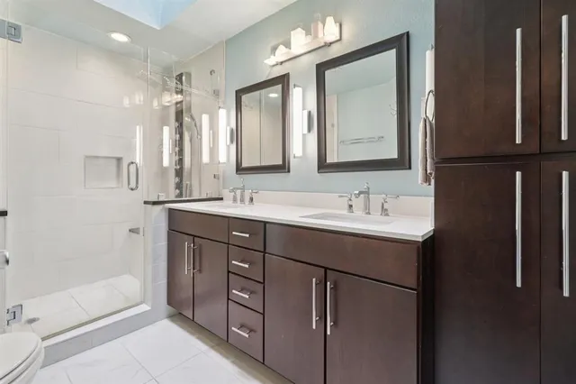 a bathroom with a double vanity sink a toilet a mirror and shower