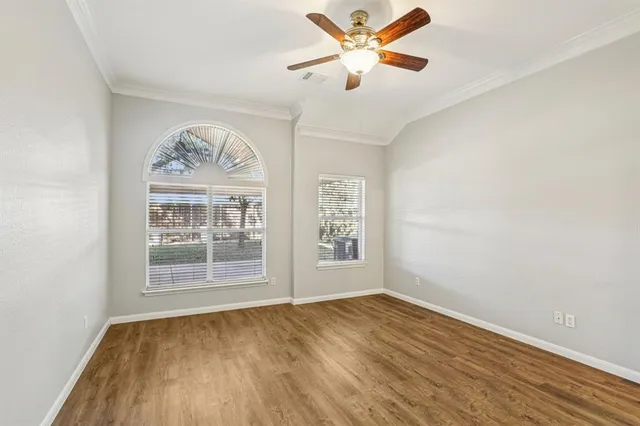 an empty room with wooden floor chandelier fan and windows
