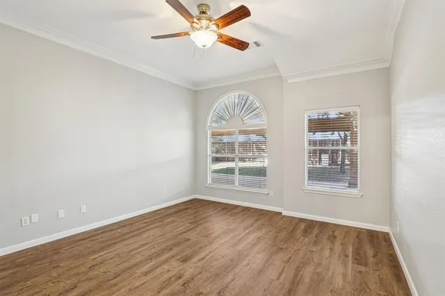 an empty room with wooden floor chandelier fan and windows