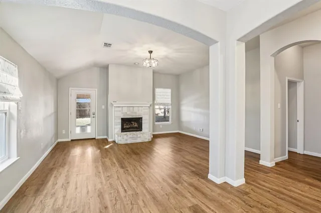 an empty room with wooden floor fireplace and windows