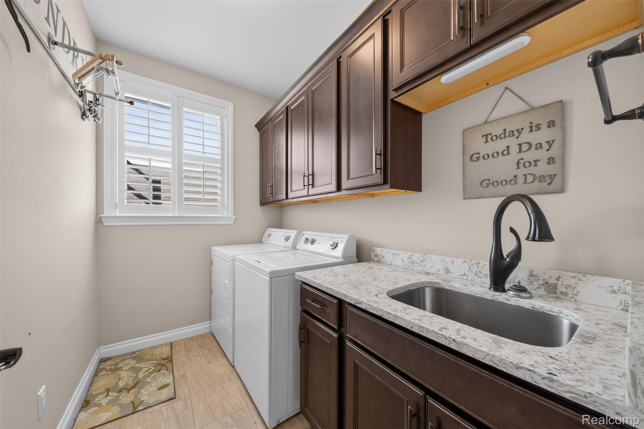 2531 Walnut View Drive Howell, MI 48855 - Photo 18 of 34 Laundry area featuring a large window with white plantation shutters, dark wood-finish cabinetry, a single basin sink with a matte black faucet, and light-toned flooring
