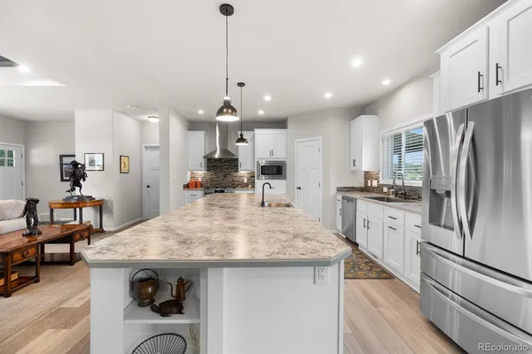 a kitchen with stainless steel appliances kitchen island granite countertop a refrigerator a sink dishwasher a stove and white cabinets with wooden floor