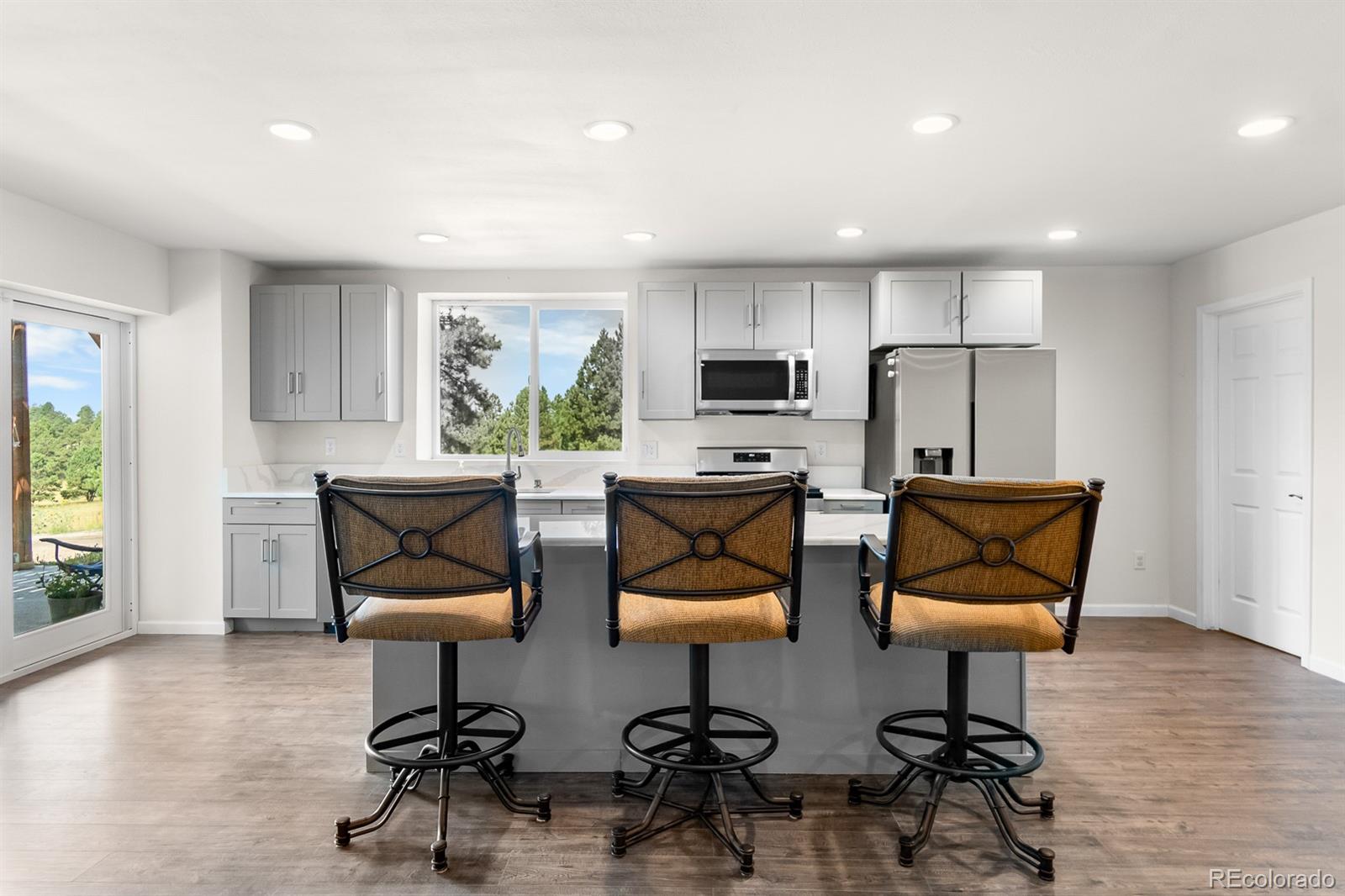 11374 Ridgewood Way Kiowa, CO 80117 - Photo 30 of 49 a kitchen with stainless steel appliances kitchen island granite countertop a stove a refrigerator a microwave a dining table and chairs with wooden floor