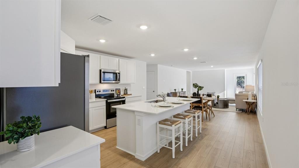 1060 Spotted Egret Loop Ruskin, FL 33570 - Photo 6 of 26 a kitchen with stainless steel appliances kitchen island granite countertop a stove a refrigerator a sink a dining table and chairs with wooden floor