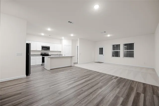 a view of an empty room with wooden floor and a kitchen