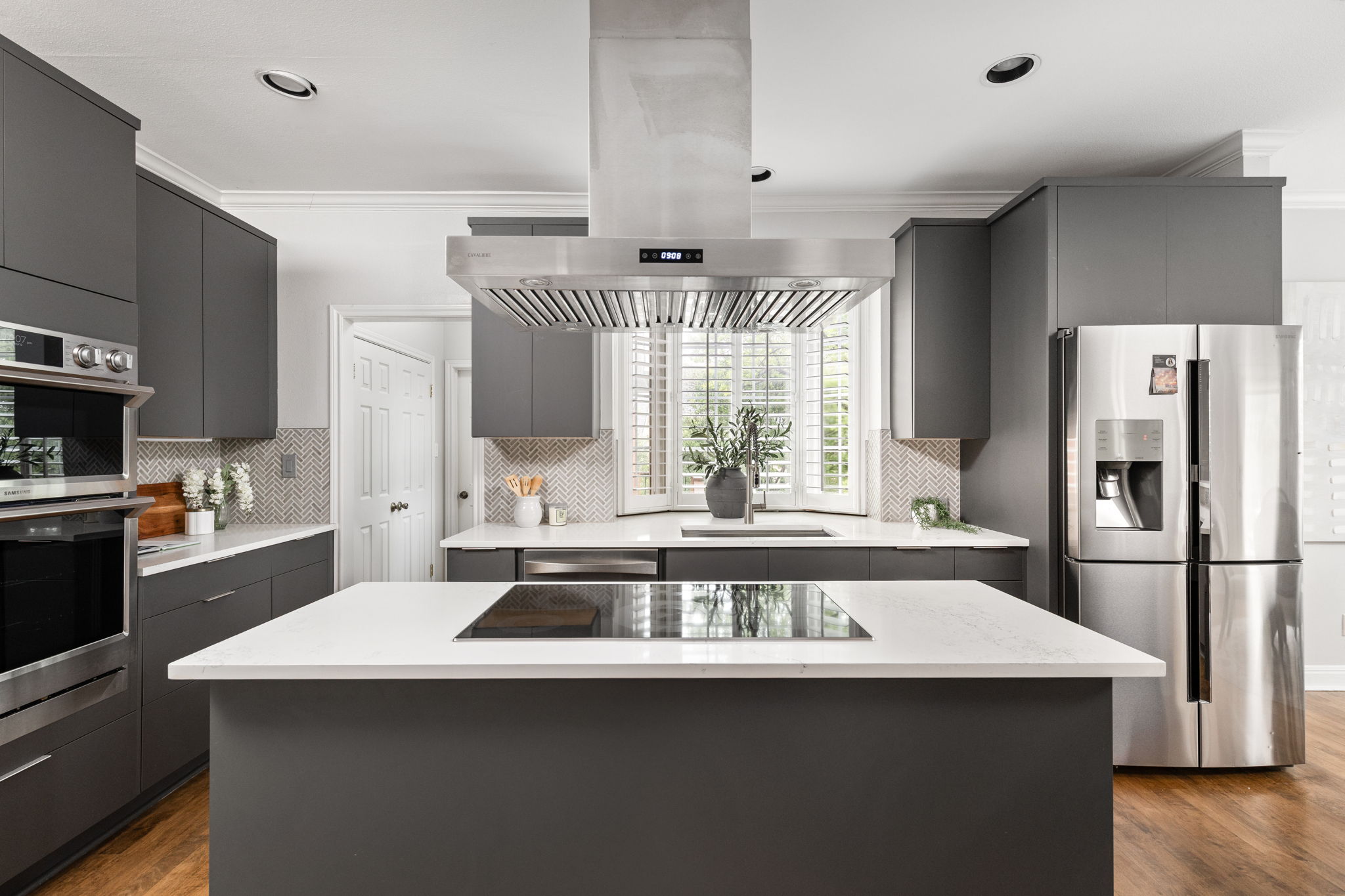 2807 Round Table Road Austin, TX 78746 - Photo 7 of 40 Modern kitchen featuring an island with an integrated cooktop, white countertops, dark gray cabinetry, stainless steel appliances, and a mosaic tile backsplash