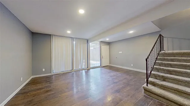 a view of an empty room with wooden floor and stairs