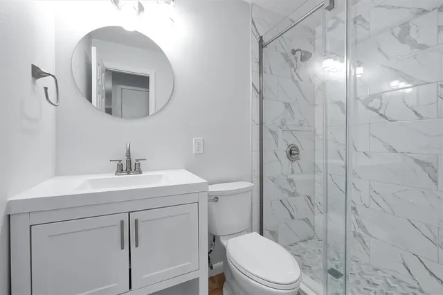 a bathroom with a toilet sink vanity granite and shower