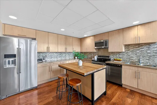 a kitchen with stainless steel appliances granite countertop a stove top oven a refrigerator a sink and dishwasher with wooden floor