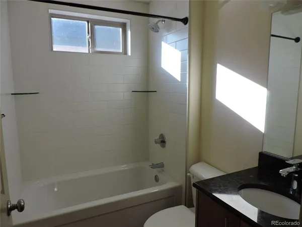 a bathroom with a granite countertop bathtub shower sink vanity and toilet