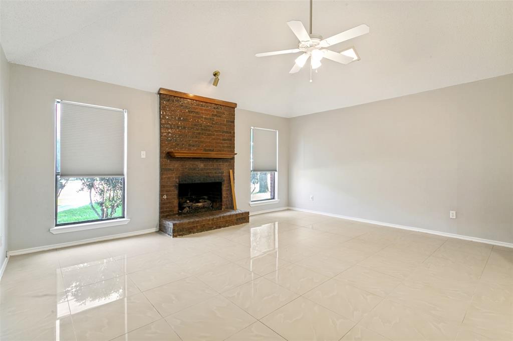 1712 East Peters Colony Road Carrollton, TX 75007 - Photo 12 of 25 Spacious interior featuring neutral paint, light-toned tile flooring, a brick fireplace with a wood mantle, and a ceiling fan with integrated lighting