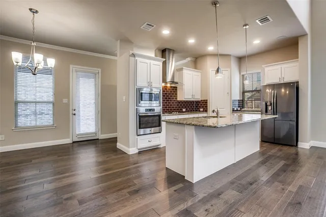 a kitchen with stainless steel appliances kitchen island granite countertop a refrigerator a oven a sink and white cabinets with wooden floor