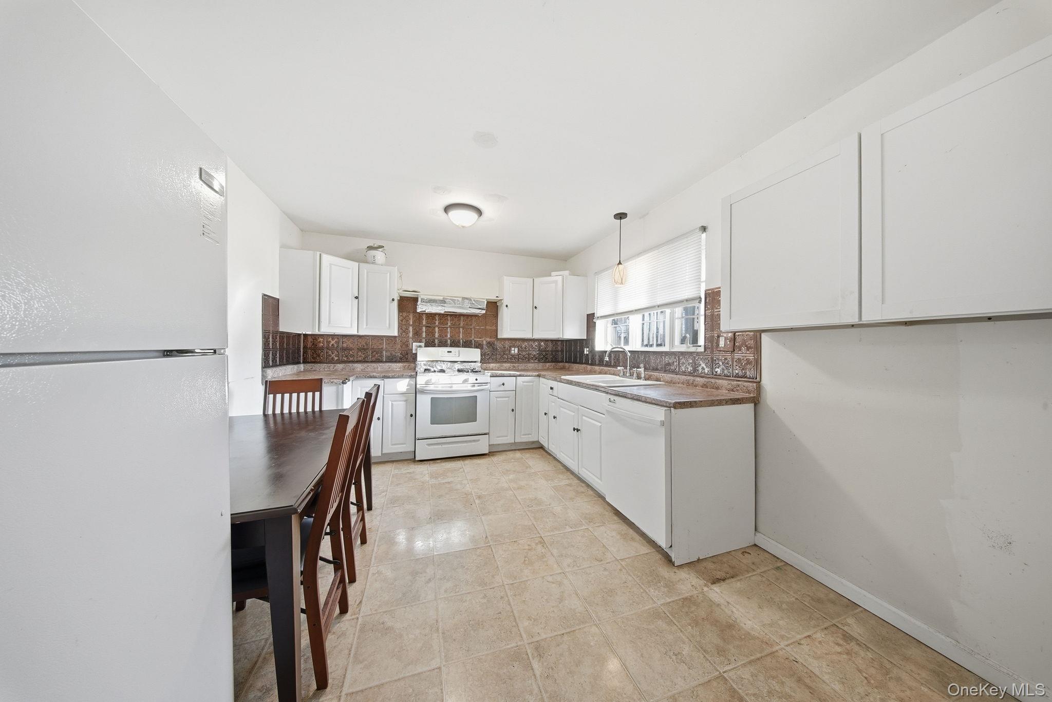21 Ridge Street Middletown, NY 10940 - Photo 12 of 32 Kitchen featuring white appliances, white cabinetry, hanging light fixtures, backsplash, and light tile patterned flooring